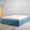A mattress on a blue bed base in a room with a wooden bedside table and hanging lamp.