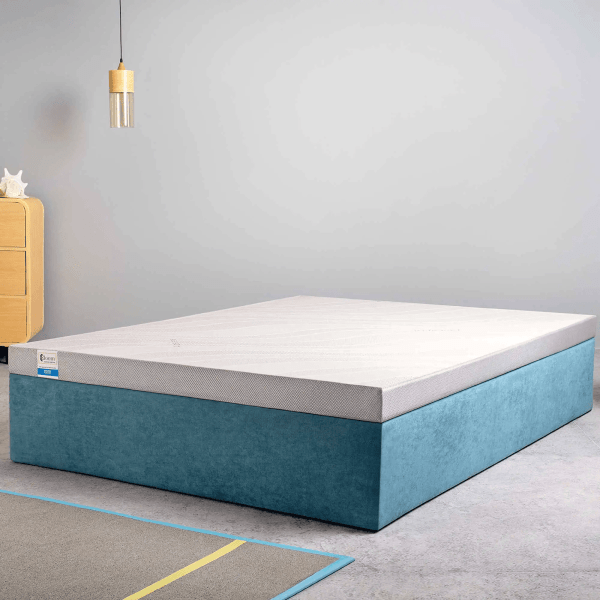A mattress on a blue bed base in a room with a wooden bedside table and hanging lamp.
